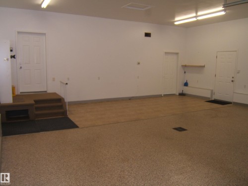 Spacious garage featuring a durable epoxy floor coating, recessed fluorescent lighting, and multiple access doors - 4825 59 Avenue, Vegreville, AB 