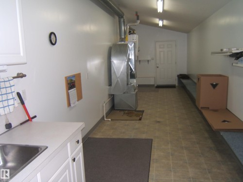 Utility area featuring a stainless steel sink, white cabinetry, light-toned tiled flooring, and permanent shelving - 4825 59 Avenue, Vegreville, AB 