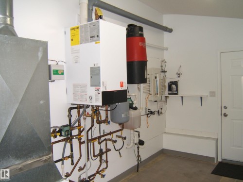 Utility area featuring a water heater, central vacuum system, and white painted walls - 4825 59 Avenue, Vegreville, AB 
