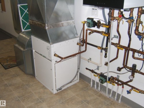 Central air handler with galvanized steel ductwork, exposed copper plumbing, and a multi-zone hydronic heating system, set on a tiled floor - 4825 59 Avenue, Vegreville, AB 