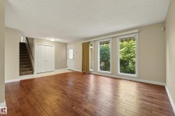 Bright, open living space featuring rich wood-finish flooring, expansive glass doors and windows with natural light, white painted interior doors, and neutral wall finishes - 
