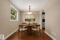 Intimate dining room showcasing warm wood-finish flooring, a round pedestal table with mid-century modern chairs, and abundant natural light from a large casement window - 