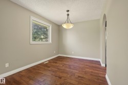Bright and spacious room featuring rich wood-finish flooring, neutral wall tones, large window with natural light, and a pendant fixture overhead - 
