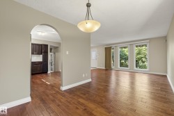 Spacious open-concept living area showcasing rich wood-finish flooring throughout, abundant natural light from multiple large windows, arched entryway with decorative trim, and pendant lighting fixture - 