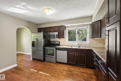 Contemporary kitchen featuring stainless steel appliances, dark cabinetry with hardware accents, wood-finish flooring, and abundant natural light from dual windows - 