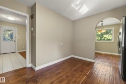 Spacious open-concept living area showcasing rich wood-finish flooring, neutral wall finishes, abundant natural light from multiple windows, and a distinctive arched doorway with polished chrome hardware - 
