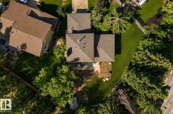 Aerial view showcasing a substantial residential property with multiple roof sections, expansive manicured lawn, mature landscaping with established trees throughout the grounds, and generous outdoor space surrounded by lush greenery - 