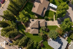 Aerial view showcasing a brick colonial residence with a steeply pitched roof, surrounded by mature landscaping including established trees and manicured lawn - 