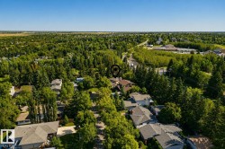 Aerial view showcasing a residential community nestled within mature tree canopy, featuring multiple single-family homes with dark-toned roofing, manicured landscaping, and established evergreen and deciduous trees throughout the neighborhood - 