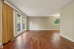 Spacious living area showcasing rich wood-finish flooring throughout, abundant natural light from multi-pane glass doors and windows, neutral wall finishes, and high ceilings with recessed lighting - 