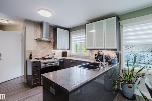 Modern kitchen featuring dark wood-finish cabinetry, light stone-finish countertops, stainless steel appliances, a tile backsplash, and wood-finish flooring - 14814 104 Avenue Nw, Edmonton, AB - Indoor Photo Showing Kitchen With Double Sink With Upgraded Kitchen