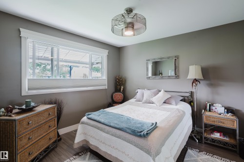 Bedroom featuring a triple-pane window with white trim, wood-finish flooring, and a ceiling fan with integrated lighting - 14814 104 Avenue Nw, Edmonton, AB - Indoor Photo Showing Bedroom