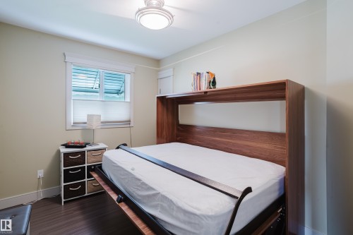 Bedroom featuring a built-in wood-finish Murphy bed with integrated shelving, wood-finish flooring, a window with blinds, and a flush-mount ceiling light fixture - 14814 104 Avenue Nw, Edmonton, AB - Indoor Photo Showing Bedroom