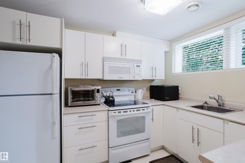 Compact kitchen featuring white cabinetry, a built-in microwave, an electric range, a stainless steel sink, and a window with blinds - 14814 104 Avenue Nw, Edmonton, AB - Indoor Photo Showing Kitchen