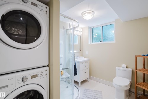 Bathroom featuring a stackable washer and dryer, glass-enclosed shower, white vanity with sink, and a commode - 14814 104 Avenue Nw, Edmonton, AB - Indoor Photo Showing Laundry Room