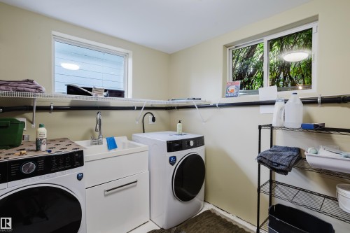 Dedicated laundry room featuring light-toned walls, two windows providing ambient light, a utility sink with a chrome faucet, and wire shelving for organization - 14814 104 Avenue Nw, Edmonton, AB - Indoor Photo Showing Laundry Room