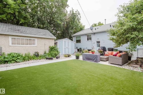 Expansive backyard featuring a large artificial turf lawn, concrete patio, detached garage with stucco exterior, and a light blue storage shed - 14814 104 Avenue Nw, Edmonton, AB - Outdoor