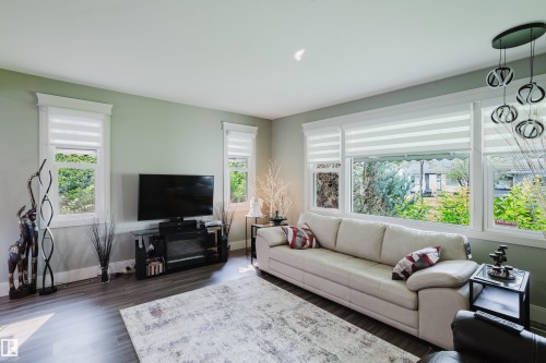 Living area featuring large windows with custom blinds, warm gray walls, wood-finish flooring, and a modern ceiling light fixture - 14814 104 Avenue Nw, Edmonton, AB - Indoor Photo Showing Living Room