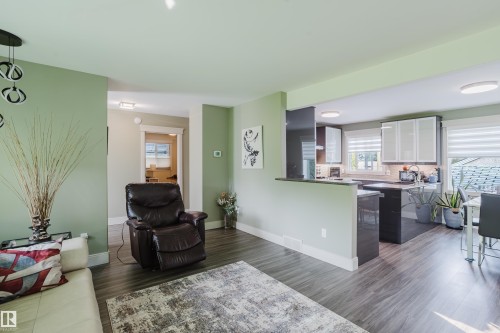 Open-concept living area featuring wood-finish flooring, a kitchen with dark cabinetry, white upper cabinets, and a kitchen island with a breakfast bar - 14814 104 Avenue Nw, Edmonton, AB - Indoor Photo Showing Living Room