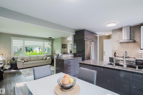 Open-concept kitchen and living area featuring dark wood-finish flooring, a kitchen island with an undermount sink, stainless steel appliances, and a tiled backsplash - 14814 104 Avenue Nw, Edmonton, AB - Indoor