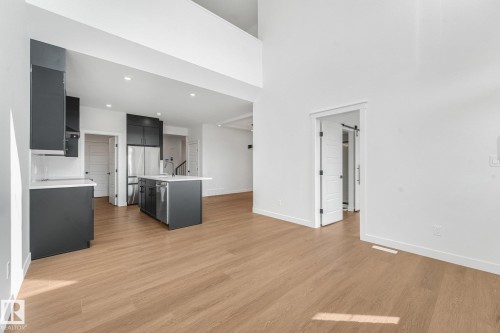 High ceilings with recessed lighting, wood-finish flooring, dark cabinetry with white countertops, stainless steel appliances, and a sliding barn door - 511 157 Avenue Ne, Edmonton, AB 