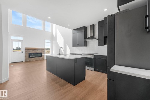 Open-concept living space with wood-finish flooring, a contemporary fireplace, and a kitchen island with sink - 511 157 Avenue Ne, Edmonton, AB 