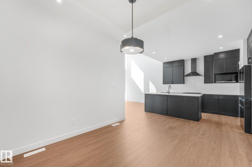 Open-concept kitchen featuring dark cabinetry, a central island with a light-toned countertop, and stainless steel appliances - 511 157 Avenue Ne, Edmonton, AB 
