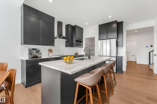 Modern kitchen featuring dark cabinetry, stainless steel appliances, a center island with a stone-finish countertop, and wood-finish flooring - 511 157 Avenue Ne, Edmonton, AB 