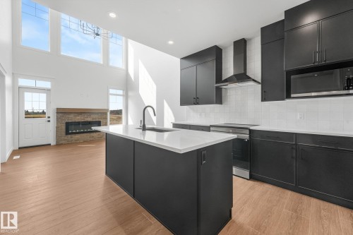 Open-concept layout with two-story ceilings, wood-finish flooring, and a modern kitchen featuring an island with a sink, black cabinetry, and stainless steel appliances - 511 157 Avenue Ne, Edmonton, AB 