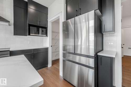 Stainless steel refrigerator, dark cabinetry, white tile backsplash, light countertop, and wood-finish flooring - 511 157 Avenue Ne, Edmonton, AB 