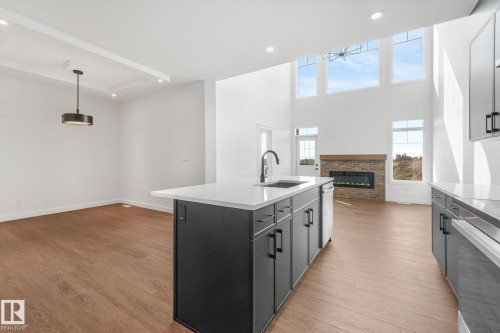 Kitchen island with a built-in sink and matte black faucet, wood-finish flooring, recessed lighting, and a fireplace with a brick surround - 511 157 Avenue Ne, Edmonton, AB 