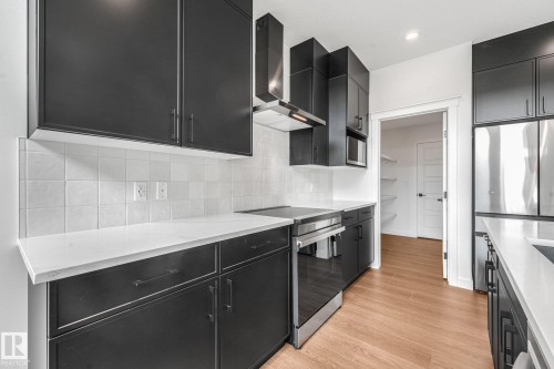 Modern kitchen featuring dark cabinetry, light-toned countertops, a tile backsplash, stainless steel appliances, and wood-finish flooring - 511 157 Avenue Ne, Edmonton, AB 