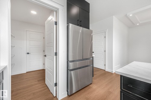 Stainless steel refrigerator, black upper cabinetry, white panel doors, wood-finish flooring, and a white countertop with grey veining - 511 157 Avenue Ne, Edmonton, AB 