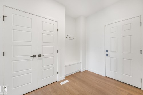 Wood-finish flooring, built-in storage bench, and white panel doors with dark hardware - 511 157 Avenue Ne, Edmonton, AB 