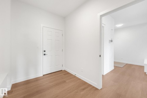 Entryway with wood-finish flooring, white walls, and a paneled door with matte black hardware - 511 157 Avenue Ne, Edmonton, AB 