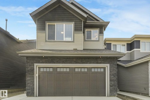 Two-story residence featuring a dark gray garage door with windows, stone veneer accents, and light gray siding - 511 157 Avenue Ne, Edmonton, AB 