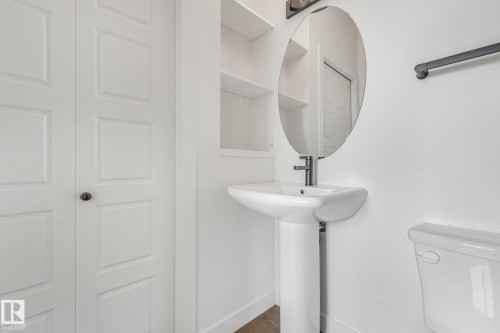 White pedestal sink with a modern faucet, oval mirror, and built-in shelving - 511 157 Avenue Ne, Edmonton, AB 