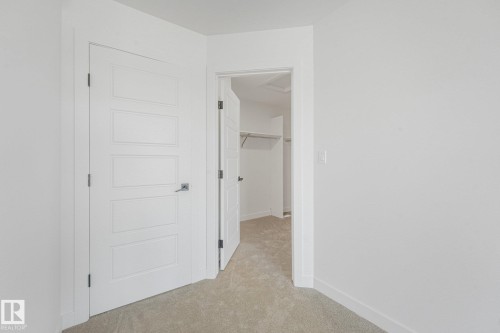 Beige carpeted flooring, white walls, and a modern five-panel interior door with dark hardware - 511 157 Avenue Ne, Edmonton, AB 