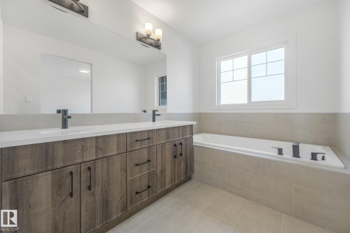 Dual vanity with wood-finish cabinetry, white countertops, and matte black fixtures - 511 157 Avenue Ne, Edmonton, AB 