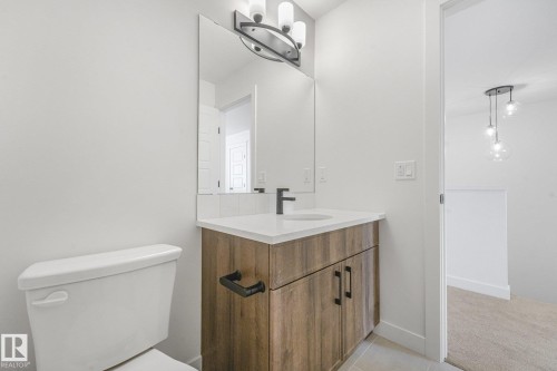 Modern bathroom featuring a wood-finish vanity with dual handles, white quartz countertop, and contemporary matte black faucet - 511 157 Avenue Ne, Edmonton, AB 
