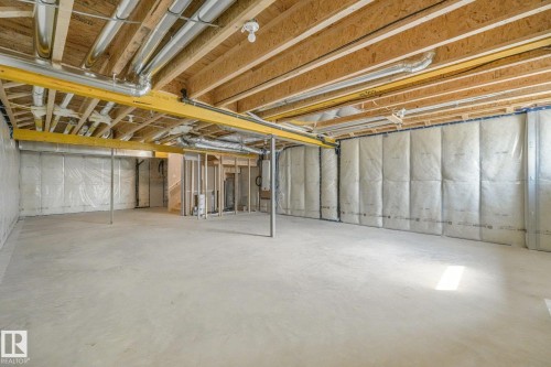Unfinished lower level with concrete flooring, exposed wood joists, structural support beams, and insulated wall framing - 511 157 Avenue Ne, Edmonton, AB 