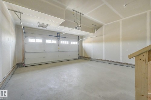 Concrete flooring, white overhead garage door with multiple window panels, exposed ceiling joists, overhead lighting fixture, interior wall shelving brackets - 511 157 Avenue Ne, Edmonton, AB 