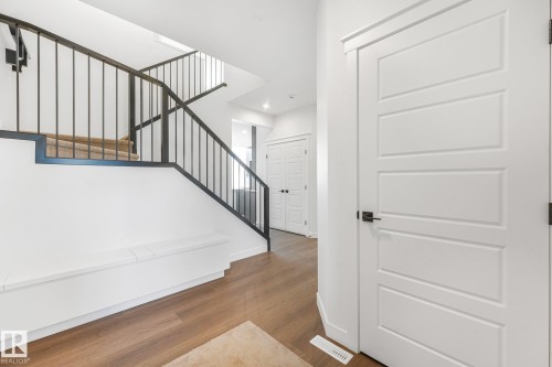 Modern staircase with black iron balusters and carpeted treads, wood-finish flooring, white panel doors, and built-in bench seating - 511 157 Avenue Ne, Edmonton, AB 