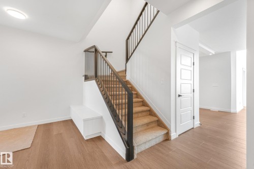 Carpeted staircase with black metal railings, wood-finish flooring, recessed lighting, and a paneled door with black hardware - 511 157 Avenue Ne, Edmonton, AB 