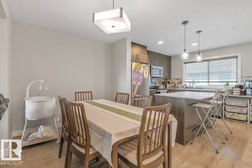 Open-concept kitchen and dining area featuring light wood-finish flooring, a kitchen island with seating, pendant lighting, and stainless steel appliances - #22 3025 151 Av Nw, Edmonton, AB - Indoor Photo Showing Dining Room