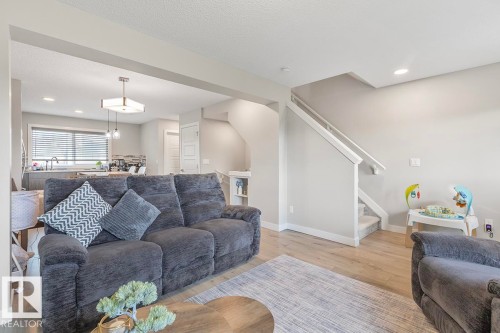 Open-concept living area featuring wood-finish flooring, recessed lighting, and a staircase with white railings - #22 3025 151 Av Nw, Edmonton, AB - Indoor Photo Showing Living Room