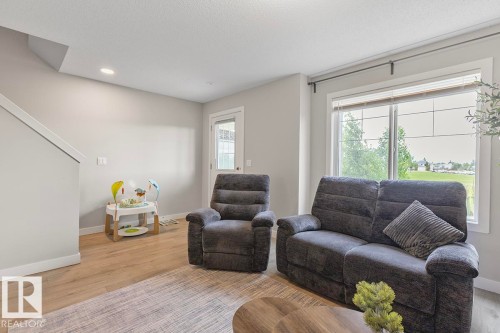 Bright living area featuring wood-finish flooring, a large window, recessed lighting, and a white interior door with glass inserts - #22 3025 151 Av Nw, Edmonton, AB - Indoor Photo Showing Living Room
