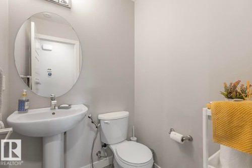 Pedestal sink with chrome faucet, oval mirror, wall-mounted light fixture, and toilet - #22 3025 151 Av Nw, Edmonton, AB - Indoor Photo Showing Bathroom