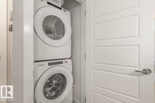 Stackable white laundry appliances within a dedicated closet, featuring a white paneled door with brushed nickel hardware - #22 3025 151 Av Nw, Edmonton, AB - Indoor Photo Showing Laundry Room