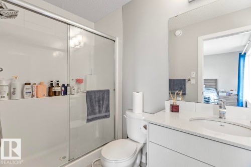 Bathroom featuring a shower with sliding glass doors, a single vanity with an integrated sink, a large wall-mounted mirror, and a white toilet - #22 3025 151 Av Nw, Edmonton, AB - Indoor Photo Showing Bathroom